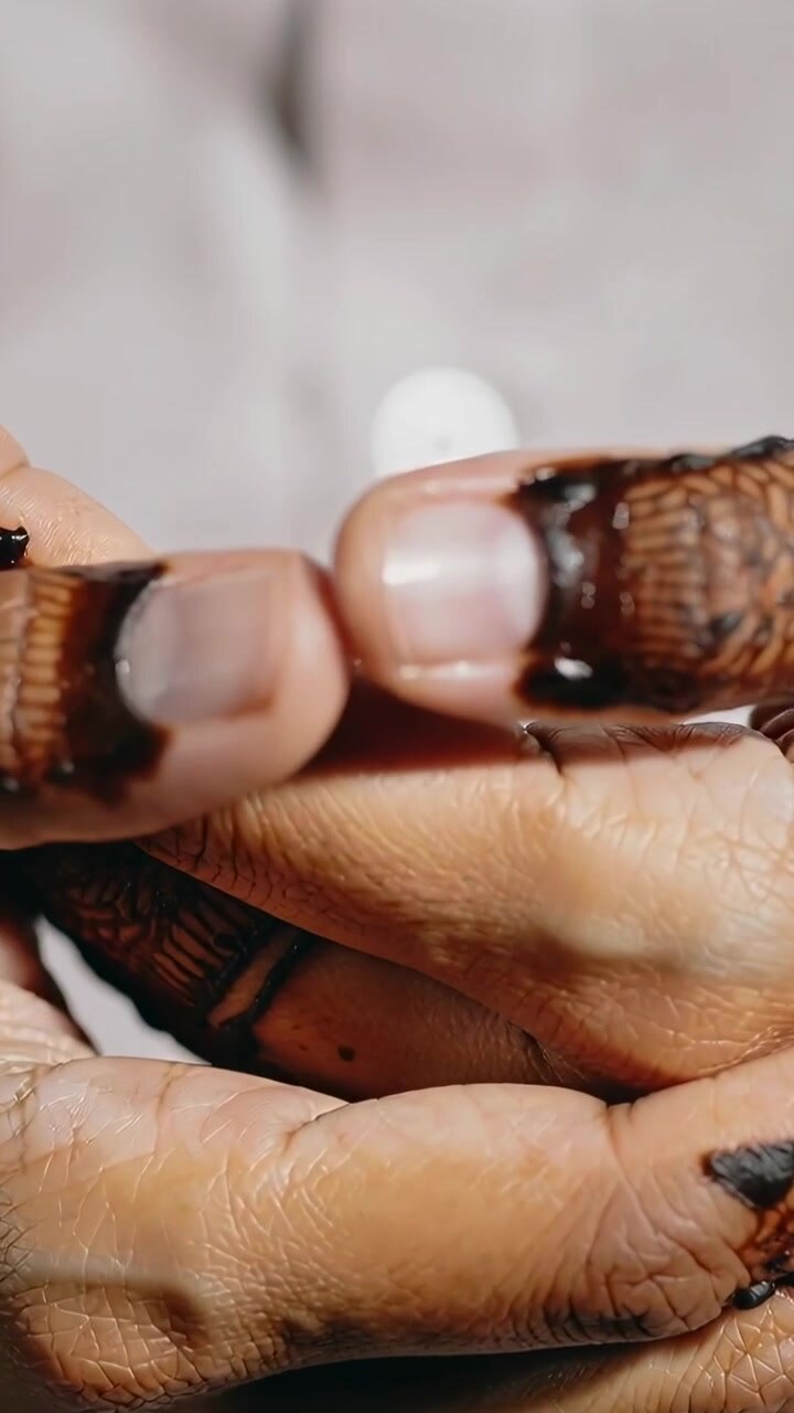 Vertical video: Camera panning hands turning thumb, shaping henna motifs, checking nails in closeup