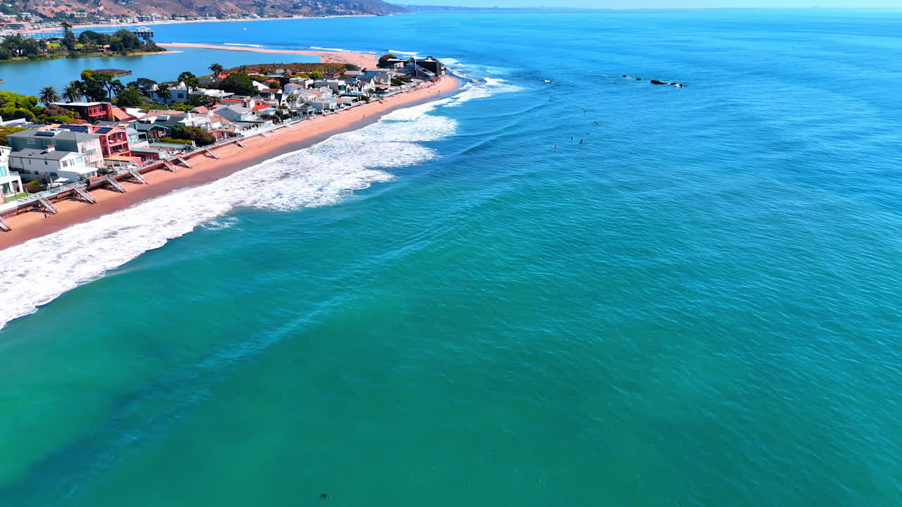 Footage over azure waterscape of the Pacific Ocean. Foamy waves roll to the houses on the beach. Malibu, Los Angeles County, California, USA