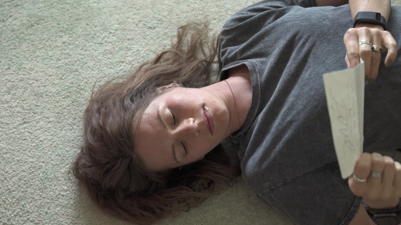 A woman lies on the ground reading a letter, absorbed in her thoughts. The camera slowly zooms in, making a gentle turning motion that captures her emotions and expressions.