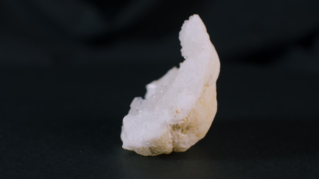 Una metà di ammasso di geode di quarzo su sfondo nero, vista in rotazione.