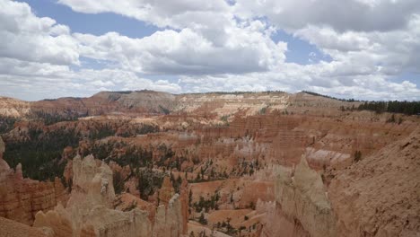 Tilt-up-shot-revealing-a-large-valley-of-orange-sandstone-hoodoo-formations-surrounded-by-greenery-and-trees-in-the-desert-of-Southern-Utah-on-a-warm-sunny-summer-day