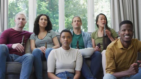 Diverse-group-of-happy-male-and-female-friends-watching-sport-drinking-beer,-cheering-in-living-room