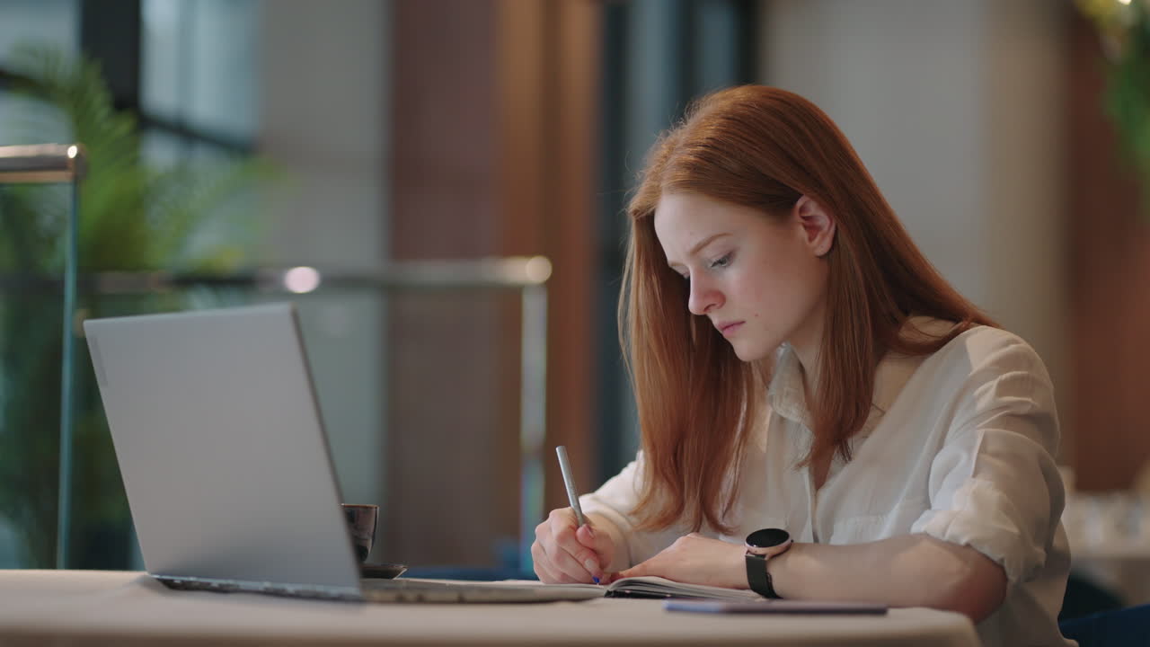 Cheerful pretty cute nice Red-haired girl girlfriend having been employed to job as executive smiling toothily sitting at desktop with laptop noting down important information
