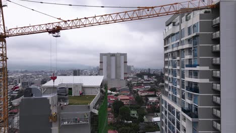 Drohnenschuss,-Der-Unter-Einem-Kran-Und-Einem-Wolkenkratzer-In-San-Jose,-Costa-Rica,-Fliegt