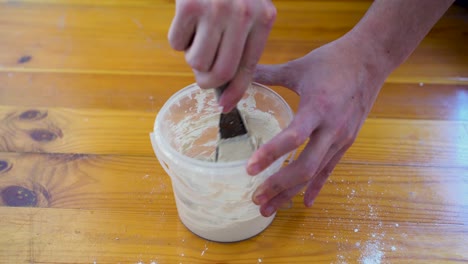 hand of person mixing putty structure in small bucket for wall repairing