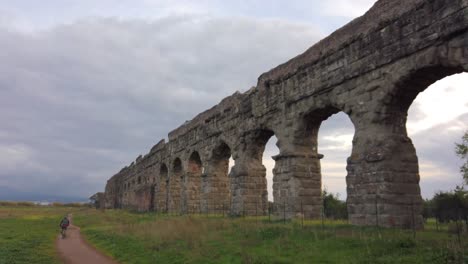 Detail-of-an-aqueduct-from-ancient-Rome-in-parco-degli-acquedotti-in-the-outskirts-of-the-capital-of-Italy,-static-shot-with-a-cyclist-passing-by