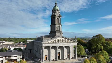 st mel's cathedral, longford town, county longford, ireland, september 2024. drone orbits counter clockwise around the restored stone roman catholic church as people past on a bright cloudy day.