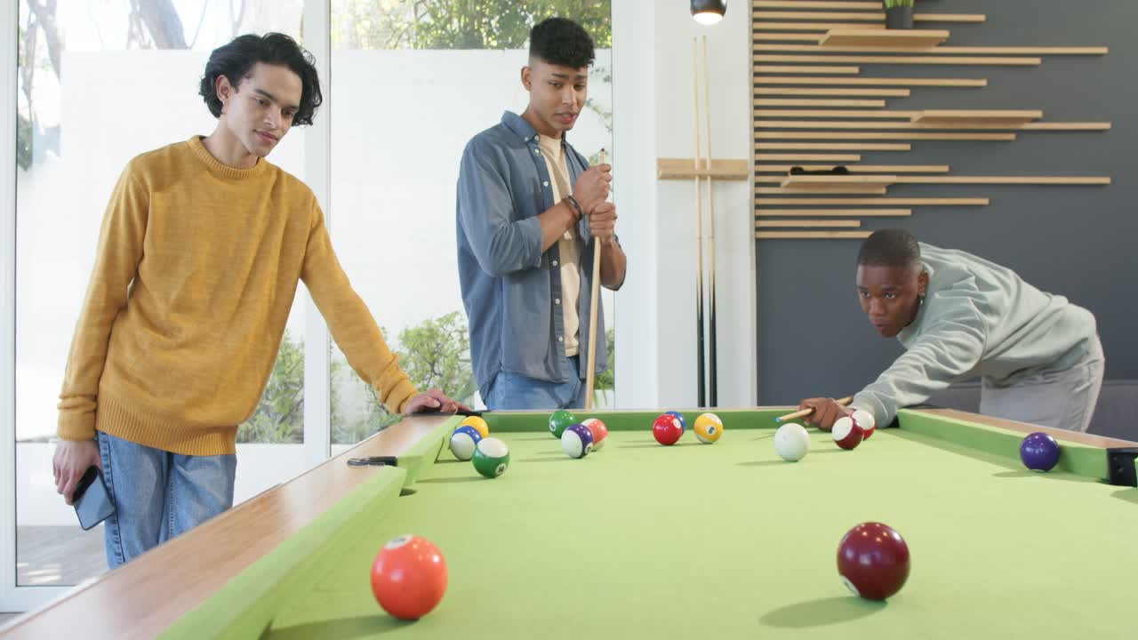 Diversos amigos do sexo masculino em mesa de bilhar, homem afro-americano alinhando e acertando a bola durante sua vez