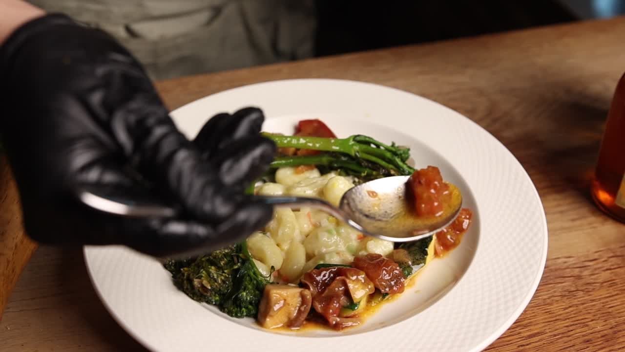 Chef's Gloved Hand Serving Gnocchi with Vegetables and Sauce