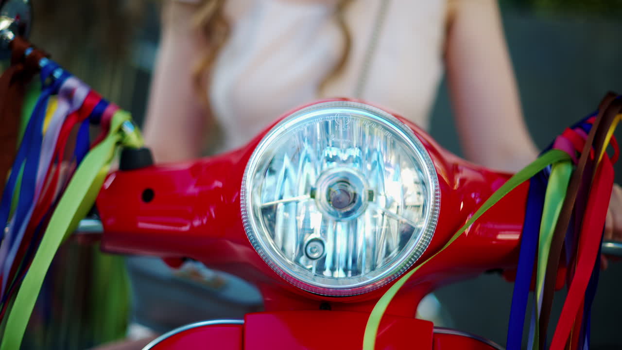 Woman standing on a red scooter with colourful decoration hanging from the mirrors