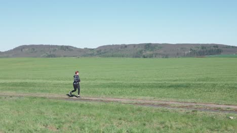 Wide,-dynamic-shot-of-a-woman-jogging-along-a-dirt-road-in-a-vast-landscape