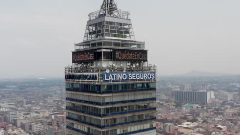 Elevated-view-of-top-floors-of-Torre-Latinoamericana-tall-building.-Drone-camera-flying-around-skyscraper,-cityscape-in-background.-Mexico-city,-Mexico.