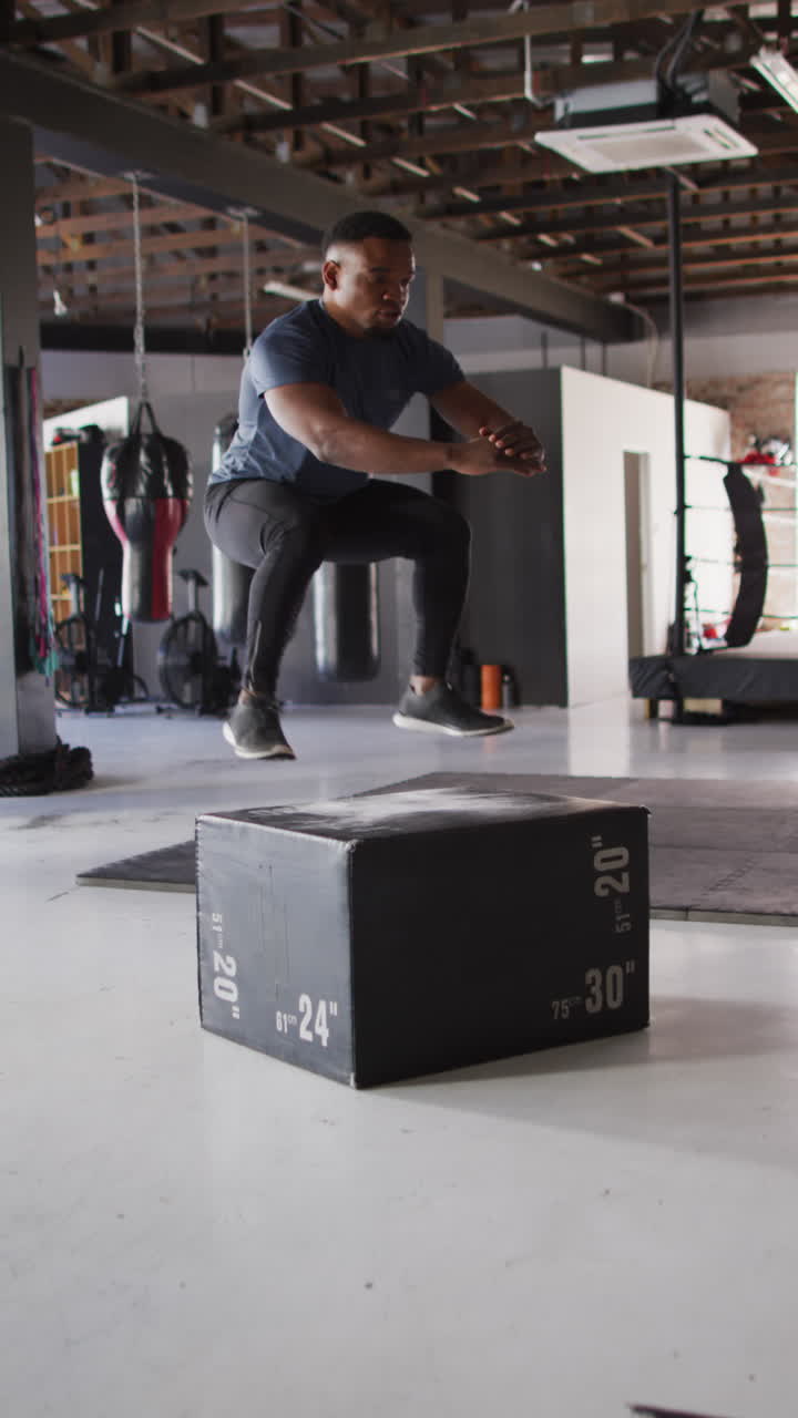 video vertical de un hombre afroamericano en forma saltando en un bloque en el gimnasio