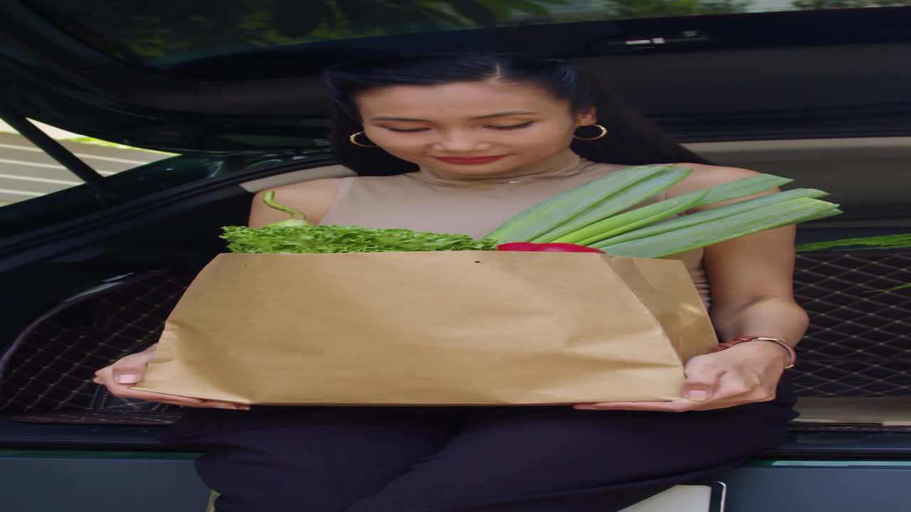 Asian Woman with Bag of Groceries Sitting on Car Trunk
