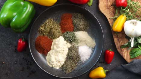 making a vibrant cajun spice blend, mixing red paprika, cayenne pepper, oregano, thyme, white garlic onion powder and black pepper in a bowl, creating a striking contrast against a black background.