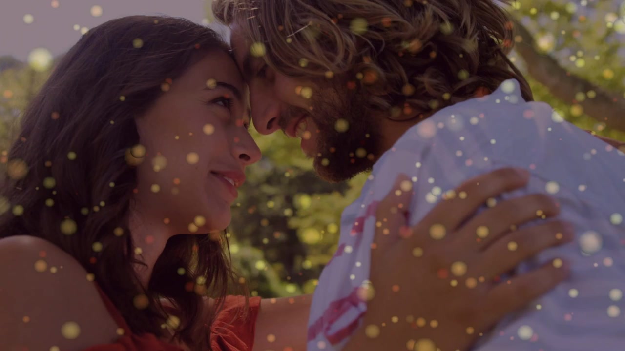 Coppia che si scambia sguardi, la donna gli tiene la spalla, l'uomo appoggia la fronte, con un'atmosfera romantica e un effetto bokeh fluttuante.