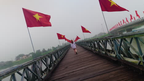 woman at hien luong bridge with vietnamese flags over hai river between south and north vietnam. - wide shot