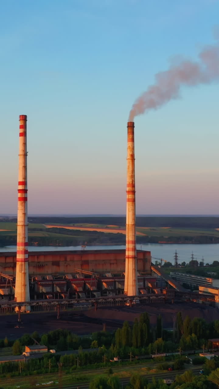 Industrial zone with chimneys at sunset. Panoramic view on pipes with smoke of factory on nature background. Environmental pollution. Vertical video