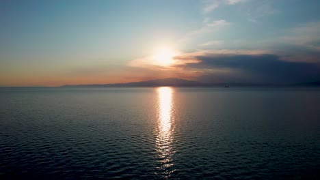 Toma-Cinematográfica-De-La-Playa-De-Prinos-Al-Atardecer,-Movimiento-Ascendente,-Cordillera-En-El-Fondo,-Cielo-Anaranjado,-Isla-De-Thassos,-Grecia,-Europa