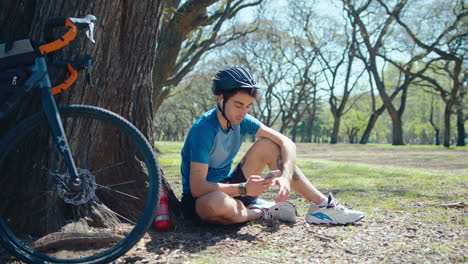 cyclist resting by tree and texting on mobile phone