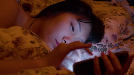 불면증을 고 있는 외로운 아시아 소녀가 밤에 침대에서 드폰으로 소셜 미디어를 검색하고 있다.