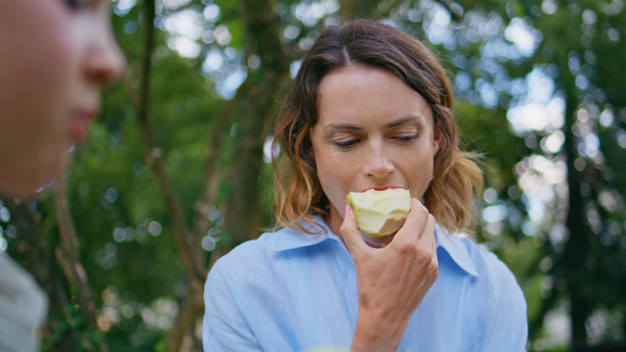 Closeup mother daughter eating apples on nature. Happy family enjoying lunch