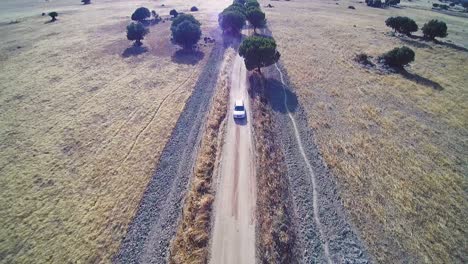 Drohnenaufnahme-Eines-Silbernen-Autos,-Das-Auf-Einer-Staubigen-Strecke-In-La-Mancha-In-Spanien-Fährt,-Sommerzeit,-Mittag