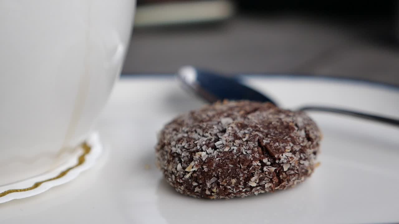 Close-up of a chocolate coconut cookie with a cup of tea and a spoon