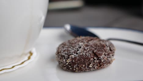 close-up of a chocolate coconut cookie with a cup of tea and a spoon