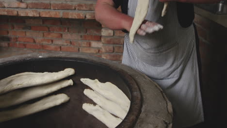 woman puts the shotis puri dough inside the traditional stone oven