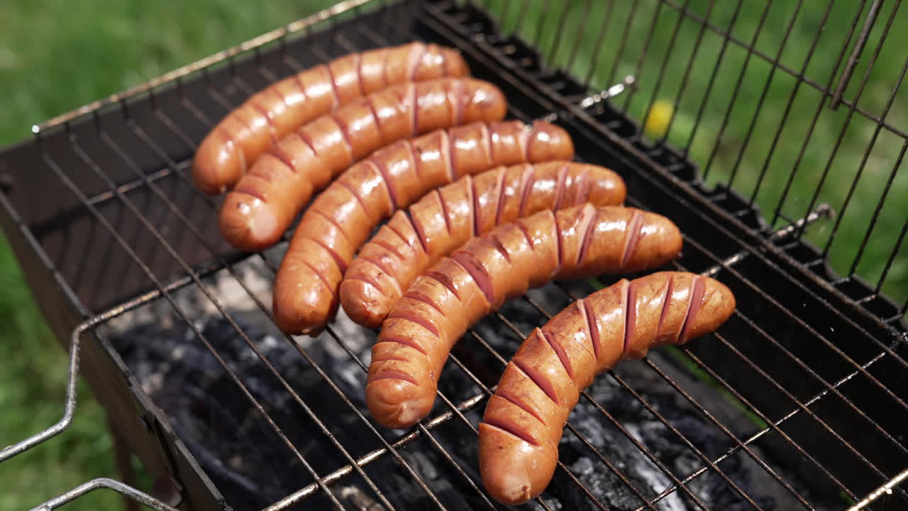 Grilled sausages roasting on barbecue grill outdoors. Grilled food frying and smoking in charcoal grills. Tasty delicious sausages. Street food for picnic and camping.