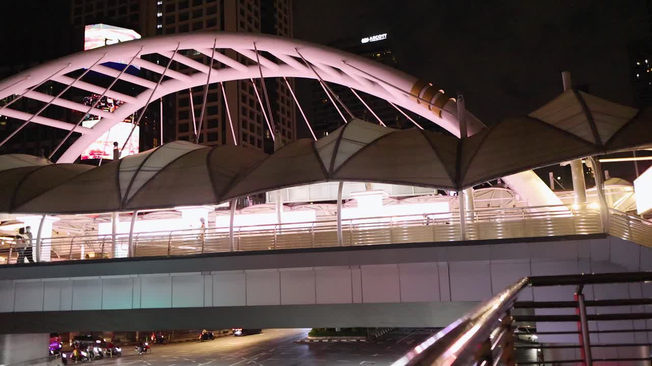 Long exposure captures moving vehicle light trails beneath modern pedestrian bridge at night