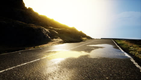 a wet road leading through a mountain pass under a bright sunset