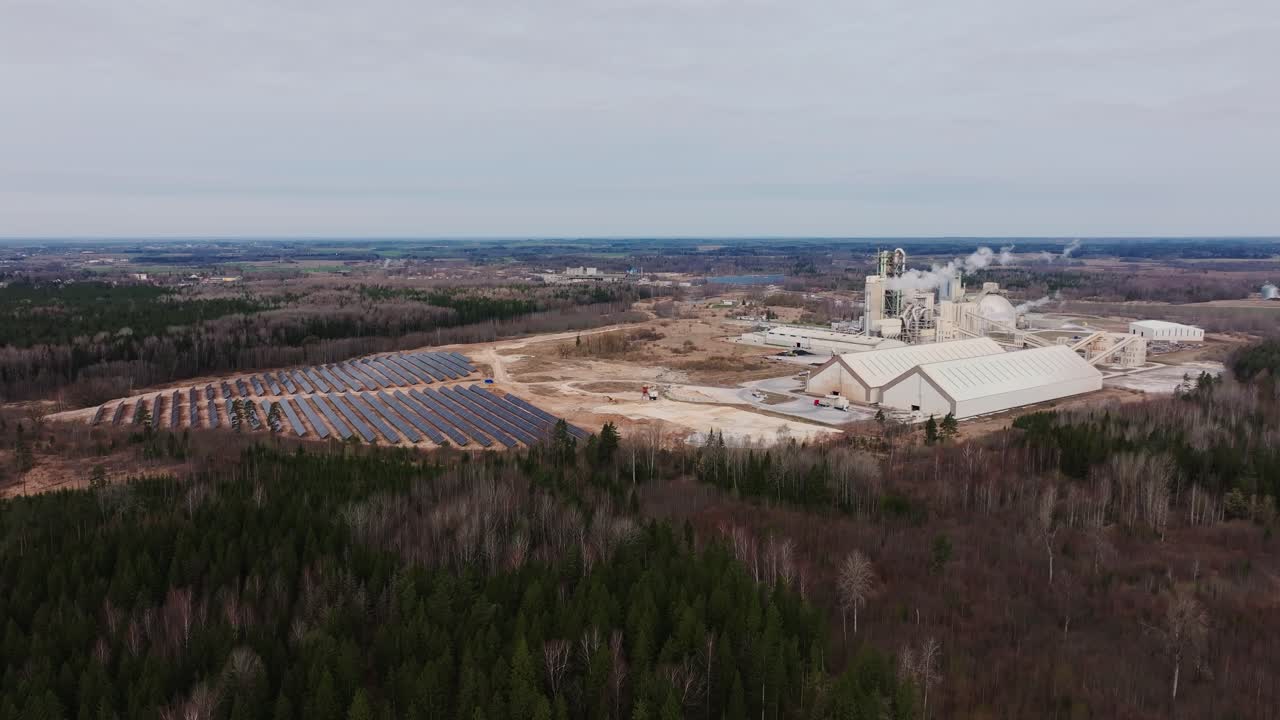 Gloomy sky hangs over solar field and smoking chimneys of remote cement plant