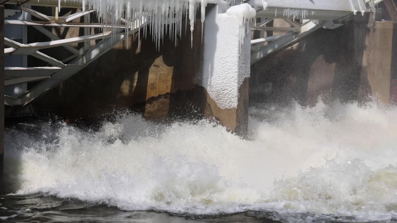 River flowing through dam with some ice on dam close up.