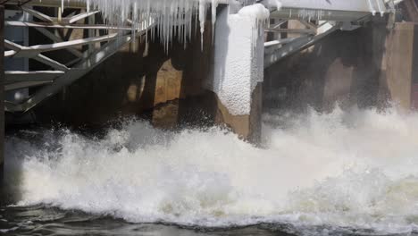 river flowing through dam with some ice on dam close up.