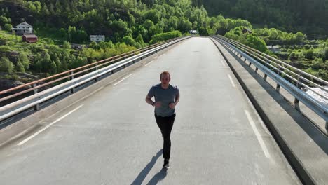 front following view of a caucasian 36 year old man jogging above countryside concrete bridge