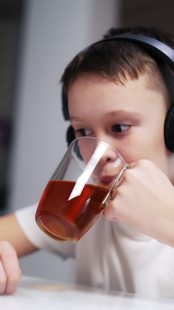 Ragazzo che guarda il tablet. Ragazzo carino che beve tè a colazione a casa mentre guarda un cartone animato sul tablet.
