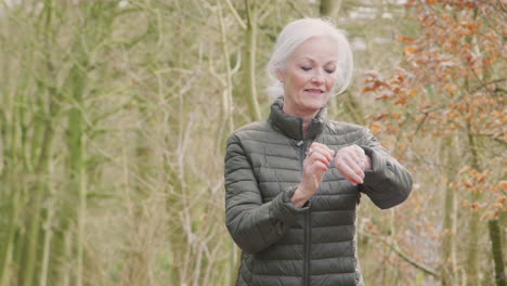 senior woman running in countryside exercising checking smart watch fitness activity app