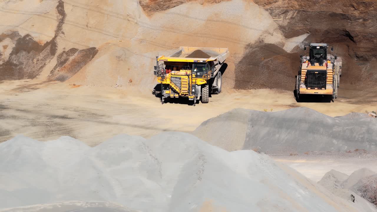 Aerial medium orbit of haul truck and wheel loader working in gravel pit, filing for transport