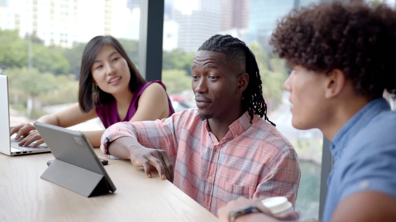 Discussing project, diverse colleagues collaborating using tablet and laptop in office