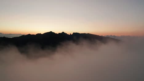 rising out of clouds revealing silhouette mountain during dawn, aerial