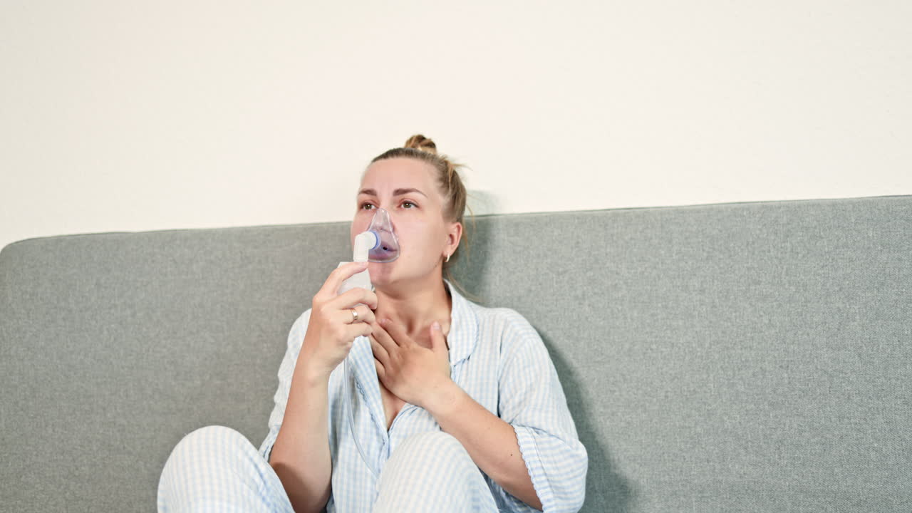 Femme malade toussant à la maison, assise sur son lit et respirant avec un nébuliseur. Femme traitant des difficultés respiratoires avec un inhalateur. Automédication à domicile.