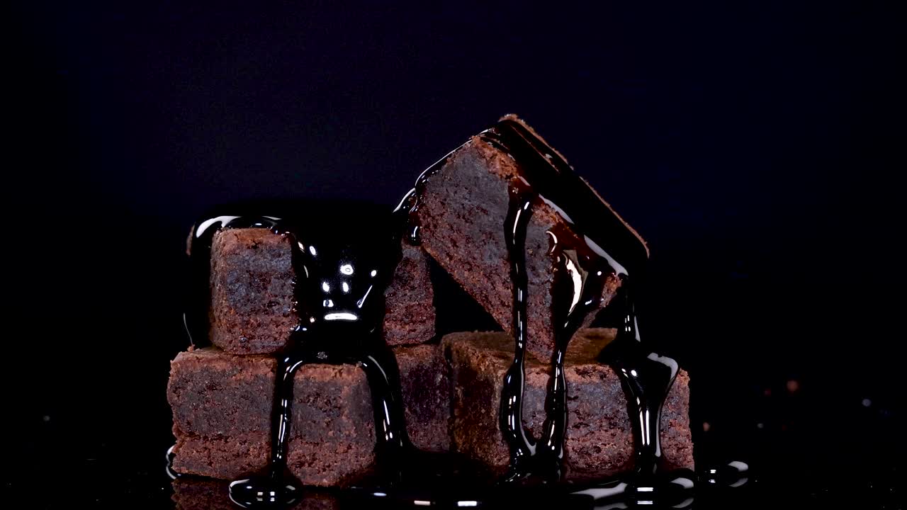 Stacked brownie cubes drizzled with chocolate sauce and rainbow sprinkles in moody studio lighting