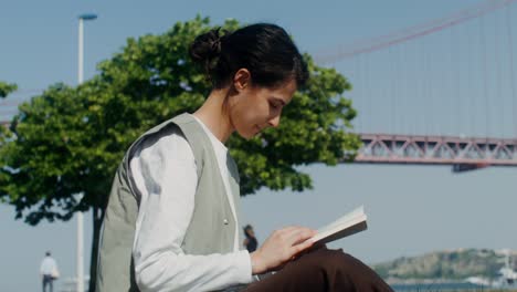 woman reading a book in a park by the bridge