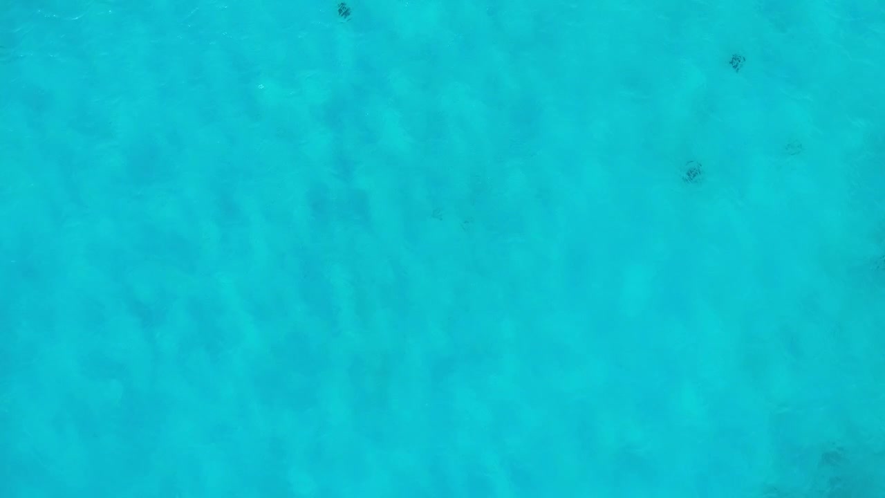 Crystal clear blue ocean water and vibrating light ripple pattern on white sand below surface, drone top down