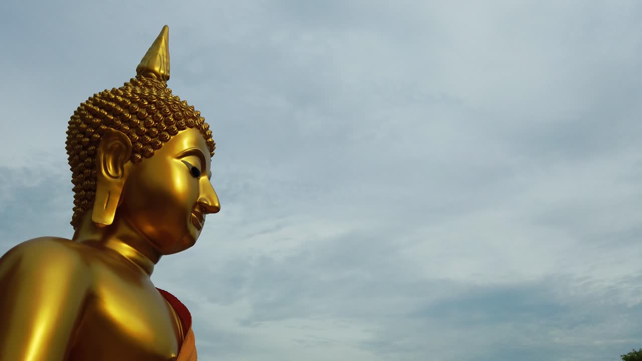 primer plano de la foto de perfil de un majestuoso dios budista divino, la estatua dorada de lord gautama buddha en un día ventoso con fondo de cielo nublado gris nublado en tailandia, sudeste de asia