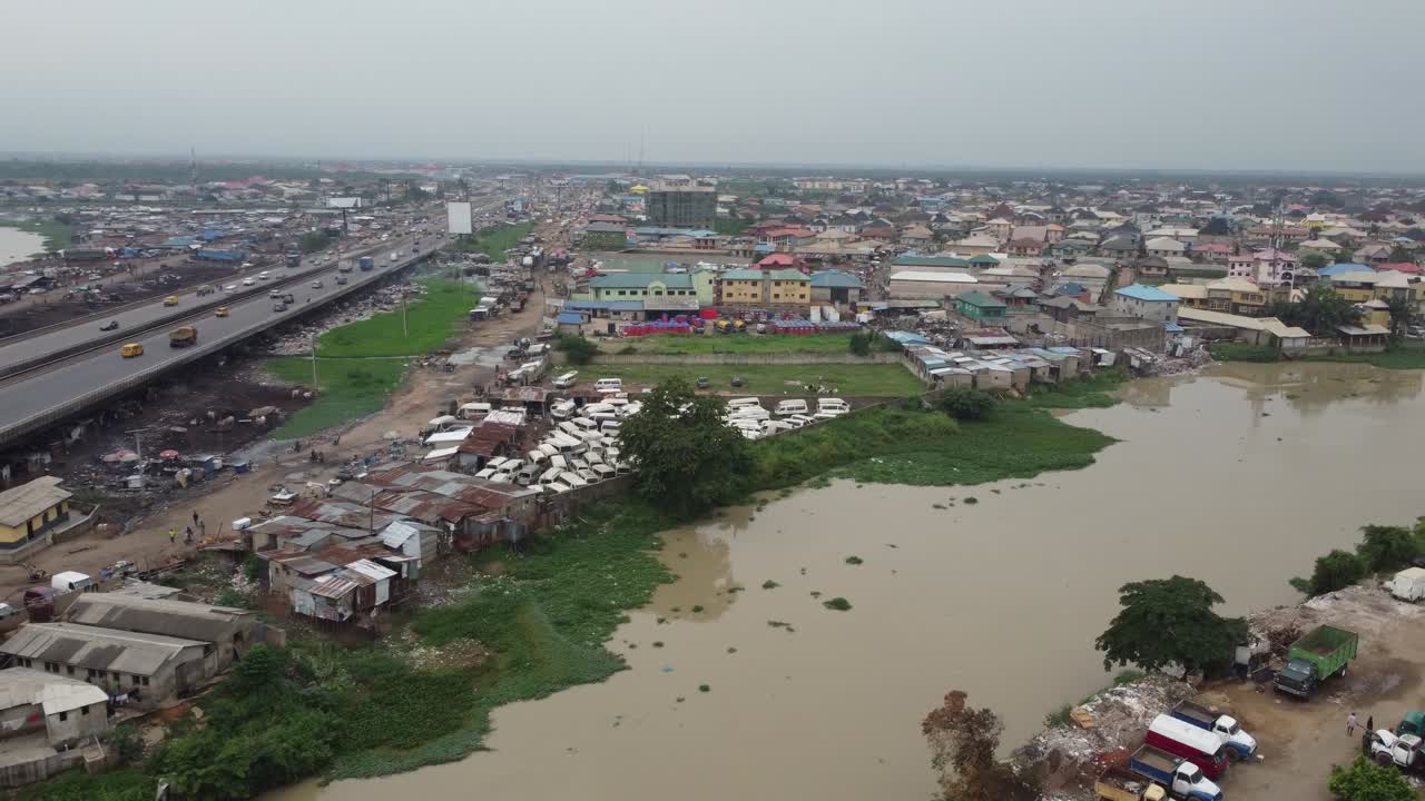 Cars moving speedily on brown river bridge of a sub-urban highway with a Nigerian flag in front of an industry