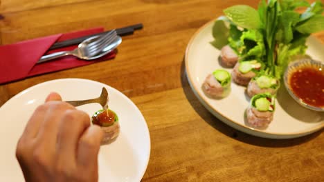 hands skillfully prepare vietnamese spring rolls with sauce on a wooden table. bright lighting enhances the fresh ingredients and vibrant colors