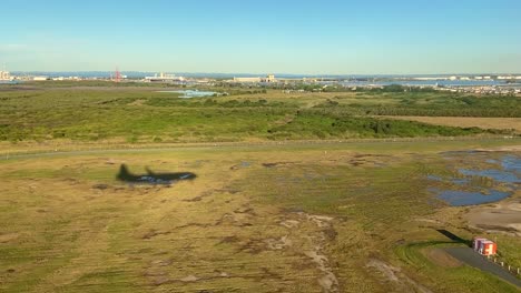 low aerial shot with shadow of landing airplane, over mangroves and marshlands with port infrastructure, waterways and coastal pools, as plane lands smoothly on the runway